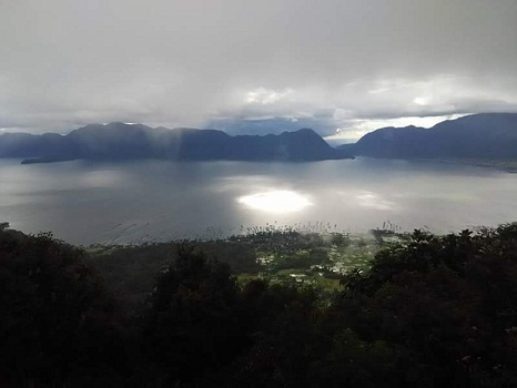Dokumentasi Foto Danau Maninjau dari Puncak Lawang:  terlihat  Air Danau Maninjau berkilauan diterpa berkas sinar matahari yang menerobos diantara celah-celah awan putih yang berarakan.